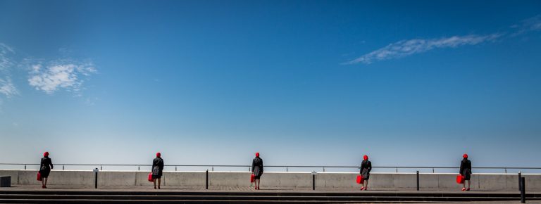 5 identical ladies in red and black looking out to the blue sky on a sunny day in Margate.