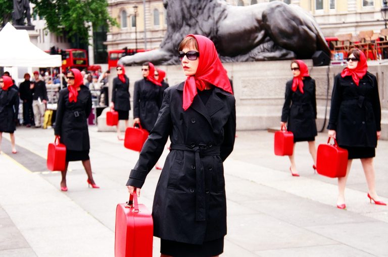 Multiple ladies dressed identically in black and red looking across Trafalgar Square