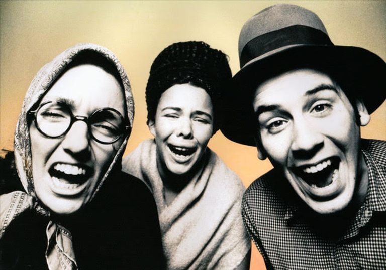 3 people in black and white laughing and looking directly at the camera in front of a orange and yellow gradient background.