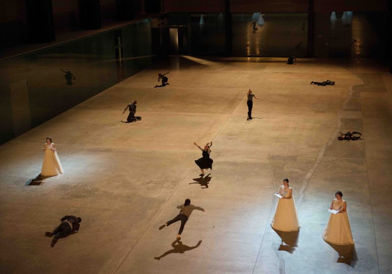 Multiple people spread out in white open dresses on a big hall floor.