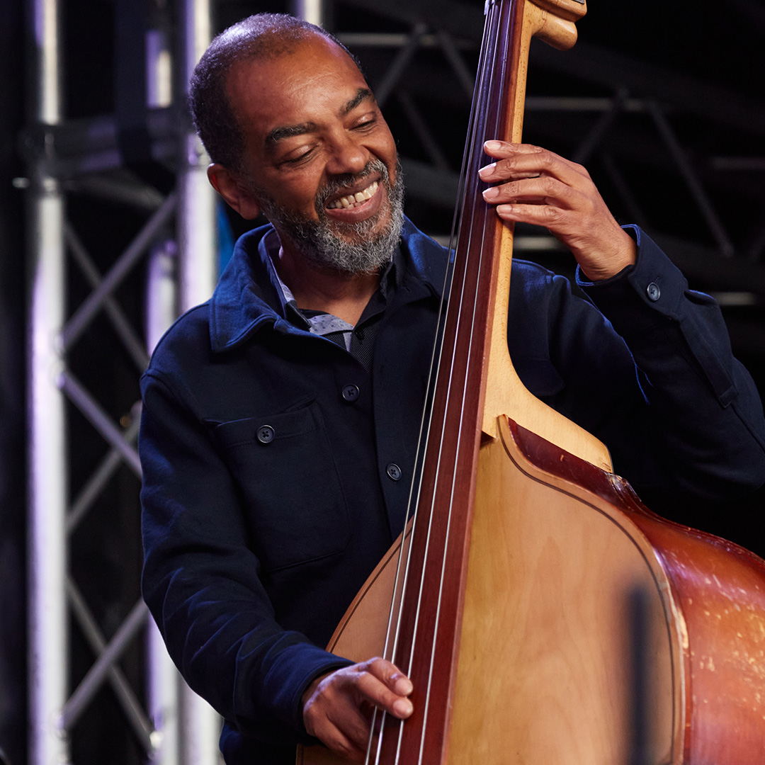 An image of Gary Crosby playing the double bass. He is looking at the bass and is smiling while he plays.