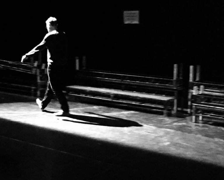 A black and white image showing a figure walking away from the camera at an angle to the left.