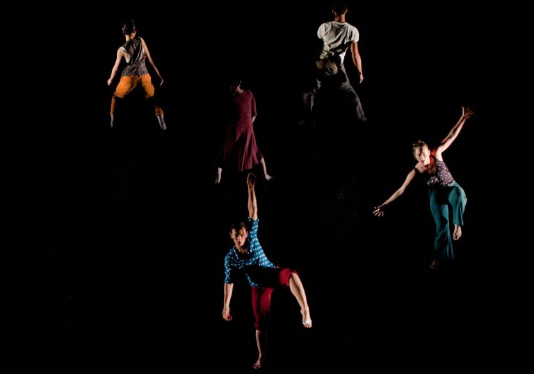 Five people spread out in different spaces wearing different colours dancing against a plain black background.