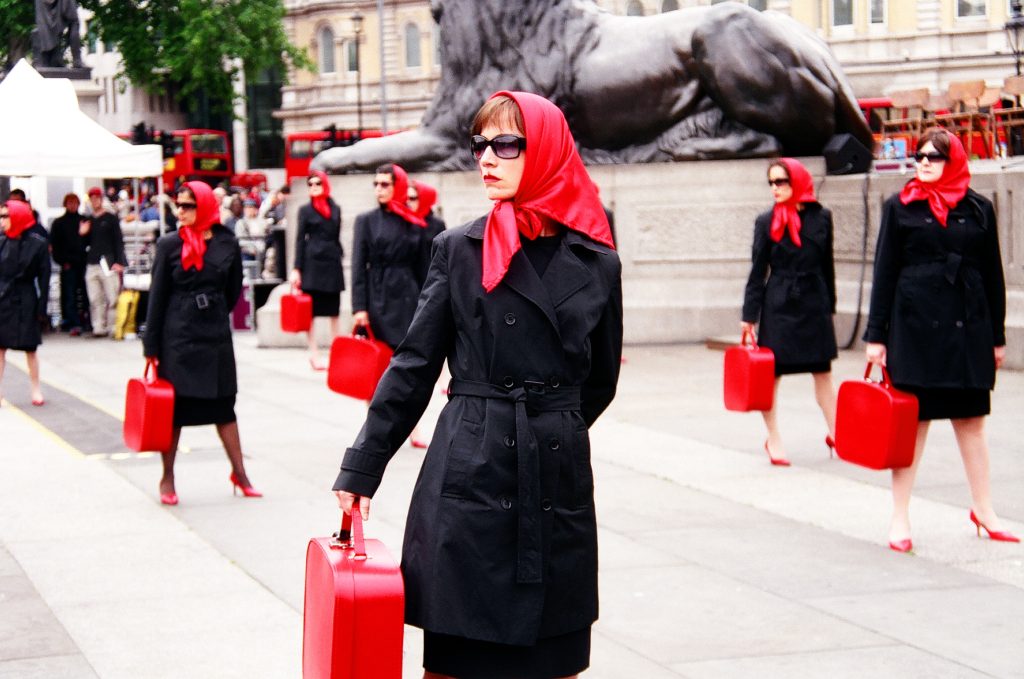 Photo from the Clod Ensemble show Red Ladies. The Red Ladies are dressed identically in the middle of trafalgar square, London 2005.
